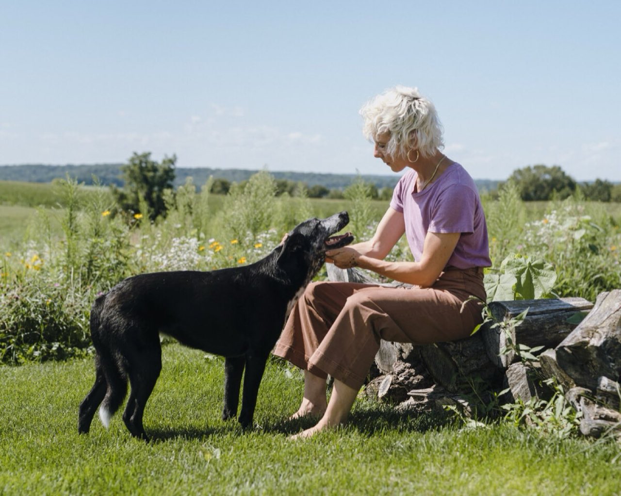 Sasha sitting with a dog in the wildflowers at the farm